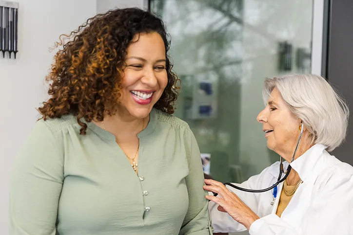 A mature woman doctor is using a stethoscope to listen to th