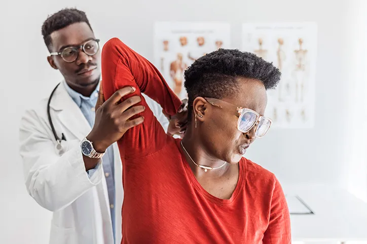 A male doctor examines the shoulder of a female patient.