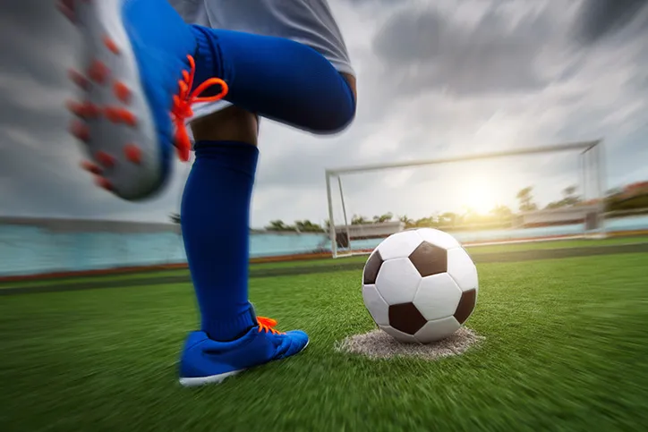 Close up of legs of a person kicking a soccer ball. The ligh