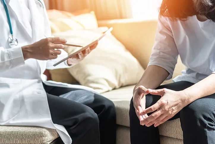 A doctor sits with a patient as they look at a tablet and ta