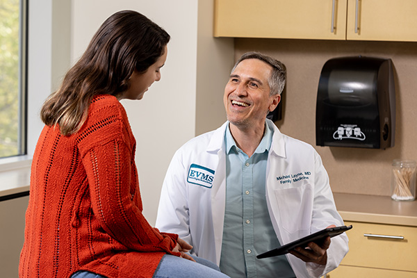 Dr. Layne talks with a patient in a clinical exam room. He is smiling and holding an ipad.