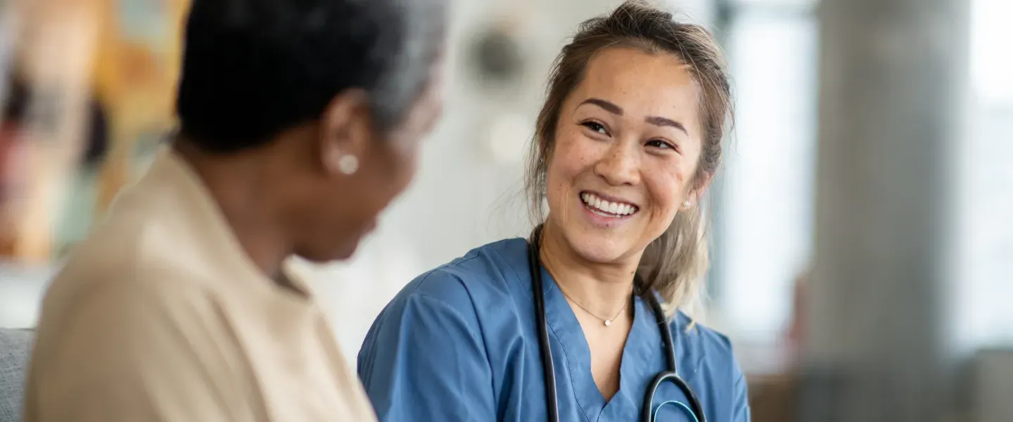 A female nurse sits with a senior patient with stethoscope o