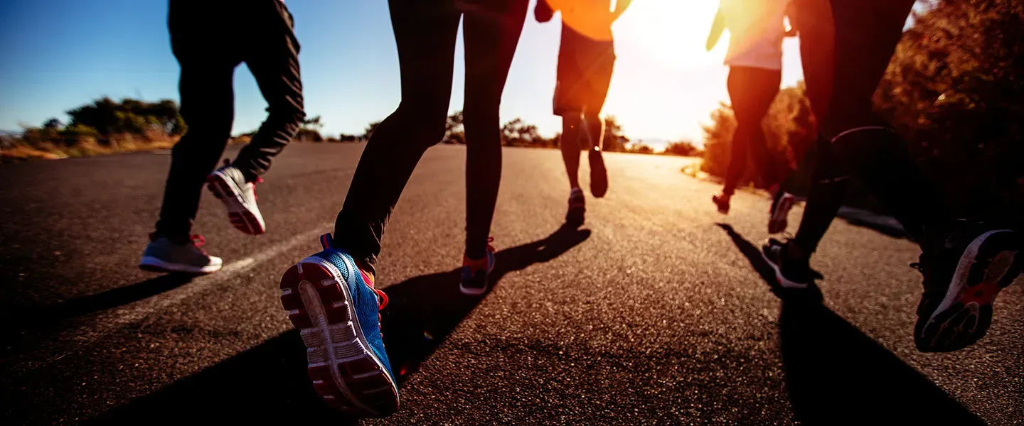 Photo of legs of runners on pavement with the sun in the bac