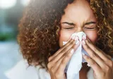 A woman has clogged sinuses and blows her nose using a tissu