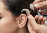 A doctor places a cochlear implant onto a woman's ear and he