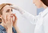 A concerned woman touches her face while being examined by a