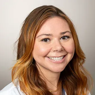 Ms. Burchett has long wavy red hair, is wearing a white medi