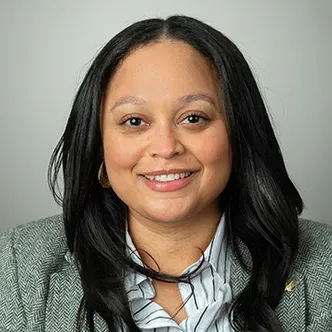 Tessa Burrus-Sanders has long wavy dark hair, is wearing a g