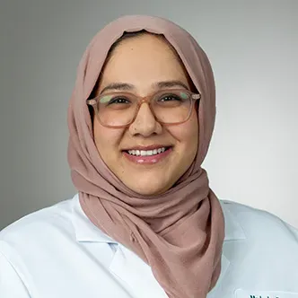 Dr. Madeeha is wearing a light mauve head covering and white