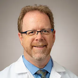 Dr. Theisz has short red hair and graying goatee, wears glas