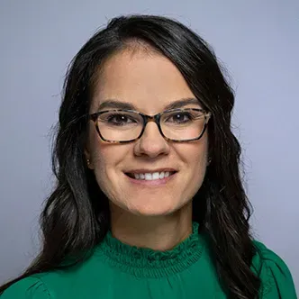 Dr. Hamersley has long wavy dark brown hair, is wearing glas