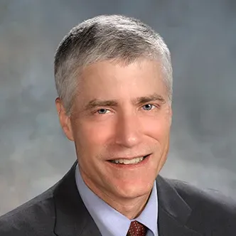 Dr. Netland has short gray hair, is wearing a gray suit with