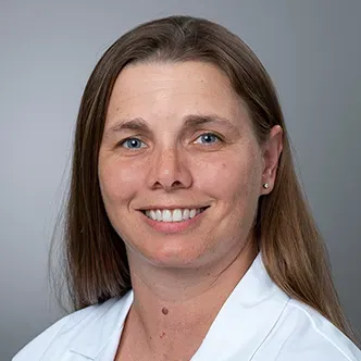 Dr. Ringwood has long, medium brown hair, is wearing a white