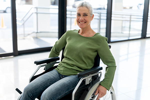 A woman wearing a green shirt smiles while sitting in a wheelchair in a clinic hallway.